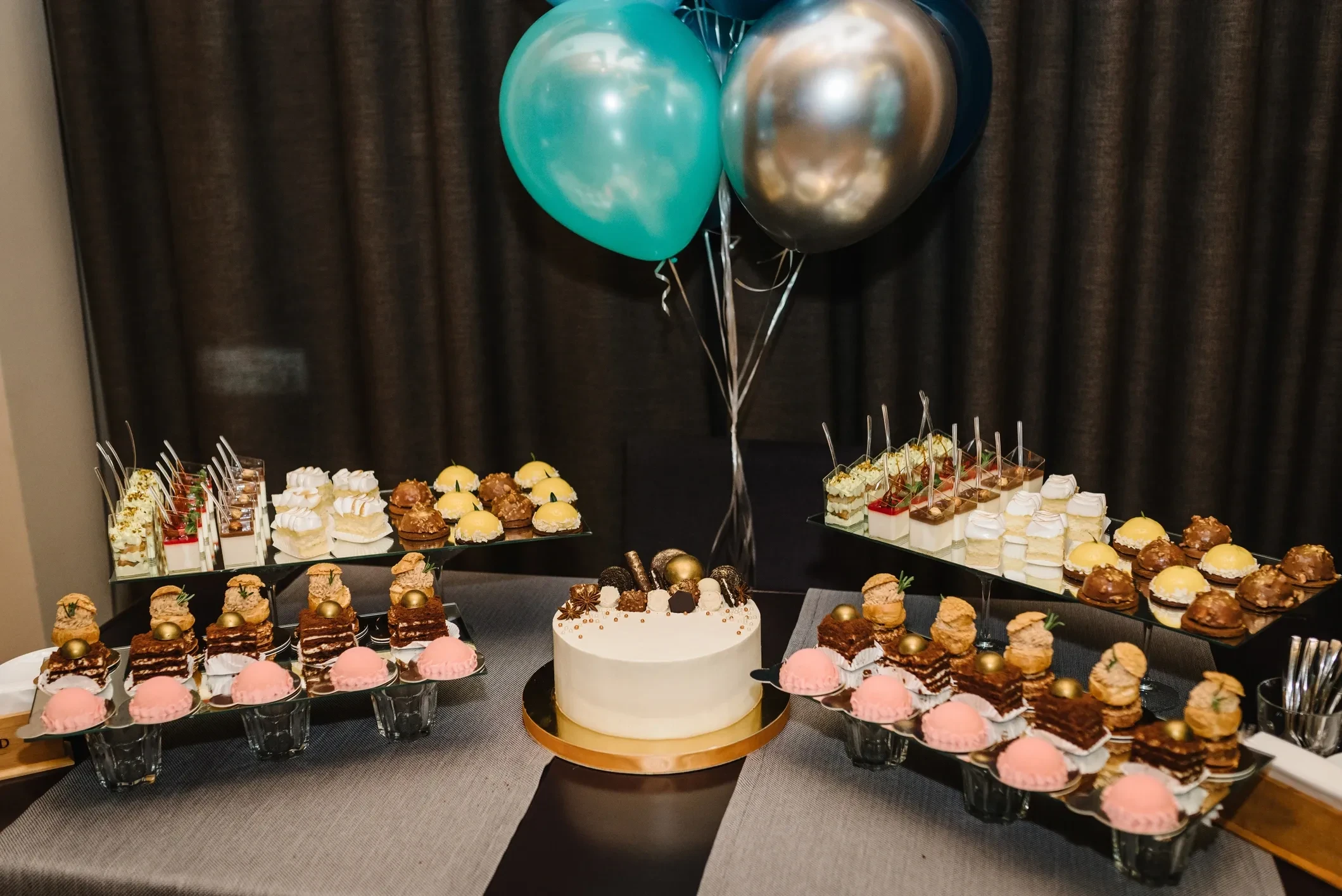 Elegant dessert table with white tiered cake, cupcake stands, and teal balloon decor catered by Asher Cuisine in Dallas-Fort Worth